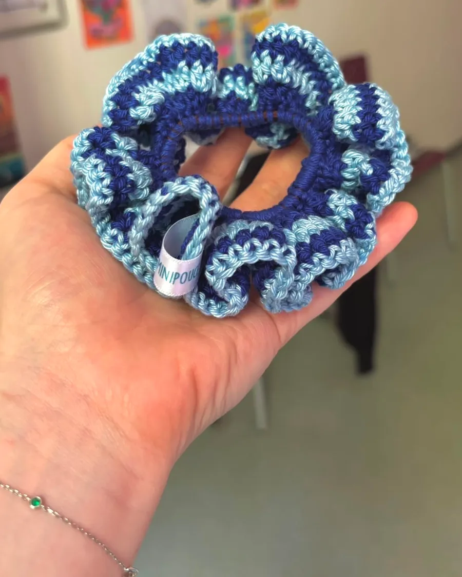 La main de Manon tenant un chouchou crocheté bleu et bleu ciel, portant l’étiquette Maison Minipouce.